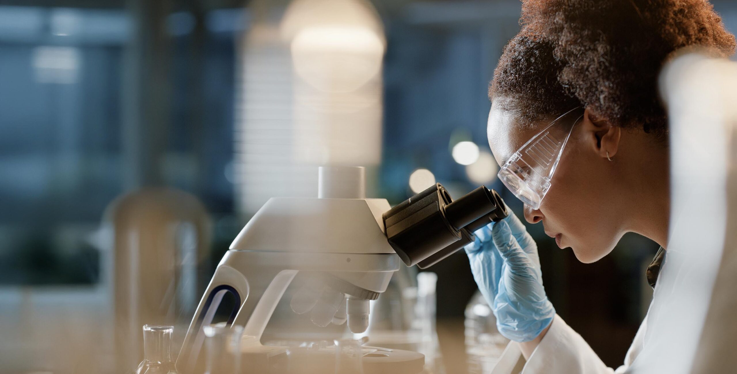 woman with goggles looking into a microscope