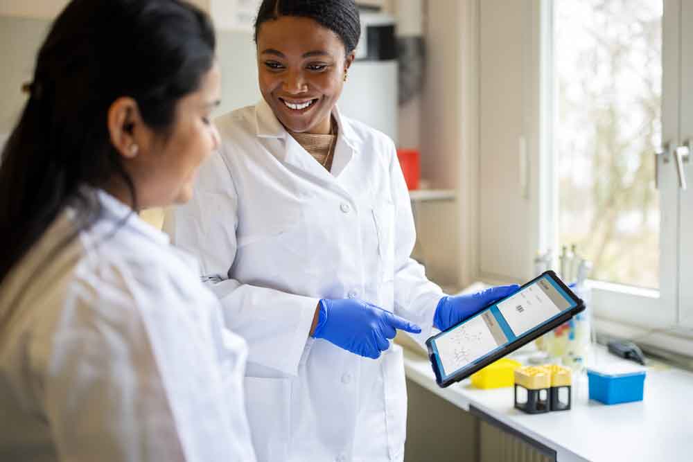 two women in lab coats looking at an ipad