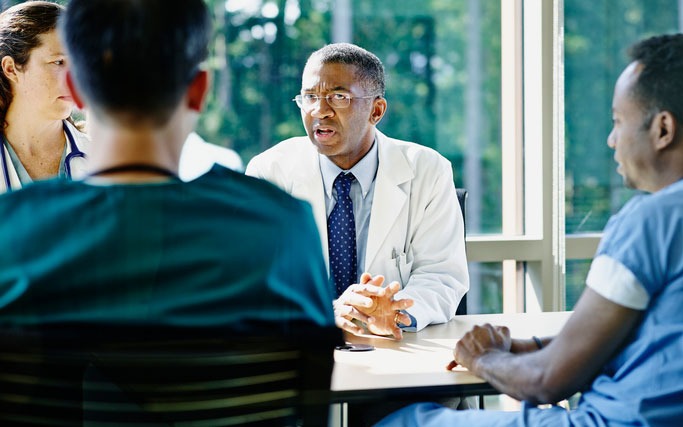 man in a white coat speaking to colleagues at a table