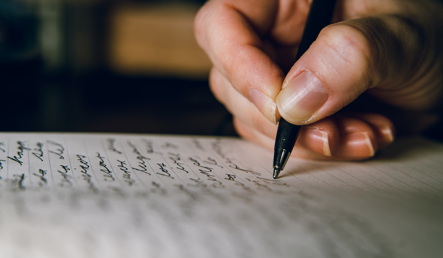 close up on a hand holding an ink pen writing on a lined piece of paper