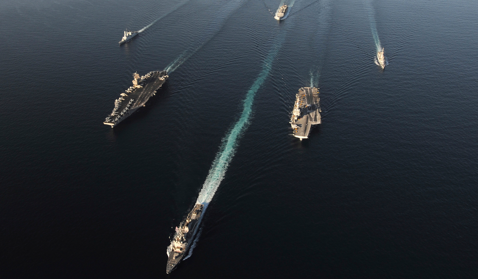 a fleet of Navy ships on the ocean, seen from the air