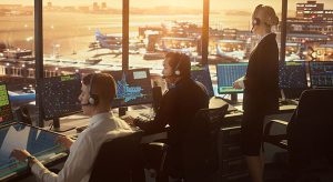 three air traffic control professionals at consoles inside a tower looking out at the runway