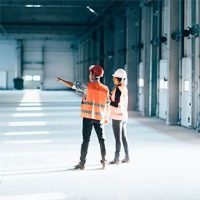 man and woman in orange vests and hard hats looking at an indoor space
