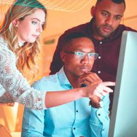 a young white woman and two young black men looking together at information on a computer