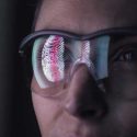 close up of woman's face with lab safety glasses that show a reflection of a fingerprint