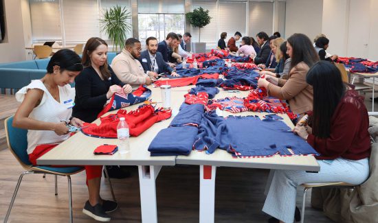 Noblis employees from the Front Line Leadership Program gathered at HQ in Reston for a community service activity, they sit at a long table cutting and tying fleece to make "Blankets for Vets."