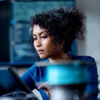 A young woman sits in a computer lab on a laptop computer performing AI system testing and evaluation.