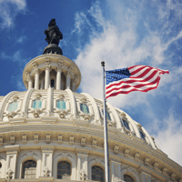 U.S. Capitol building dome with American flag flying against a blue sky.