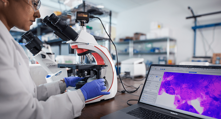 woman looking into microscope with image shown on computer screen