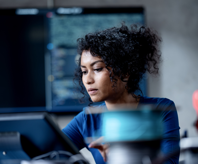 a woman sits in front of a computer in a lab looking at AI system data