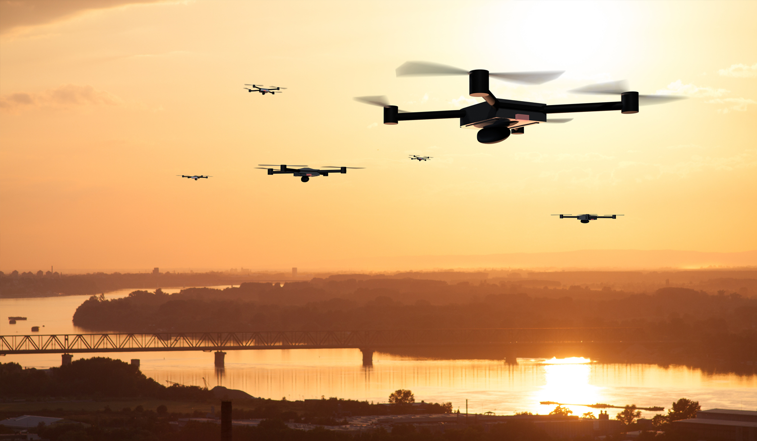 Group of autonomous drones flying over a city and river at sunset