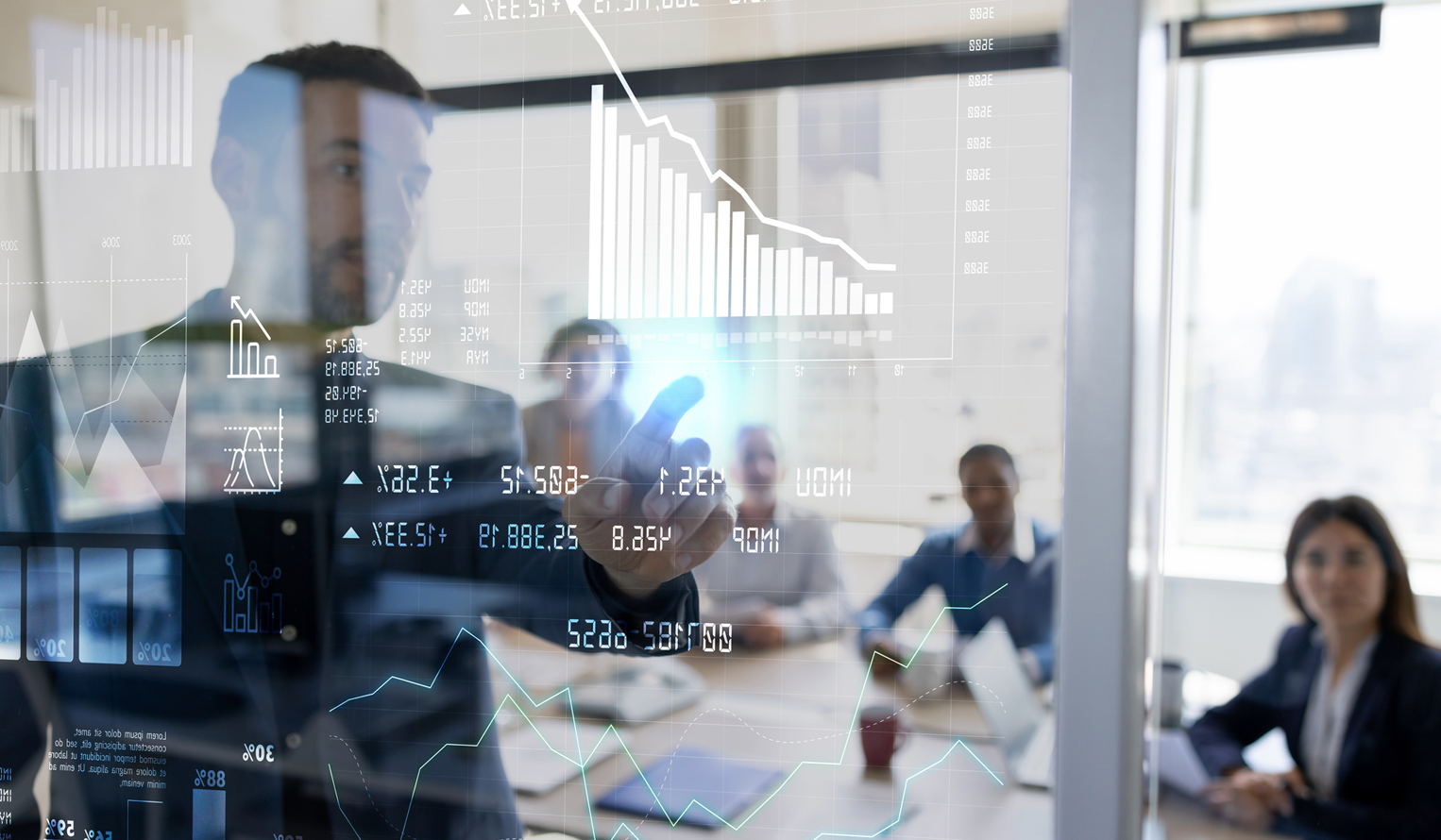 A group of people in a conference room looking at a man presenting data and results on a large clear board