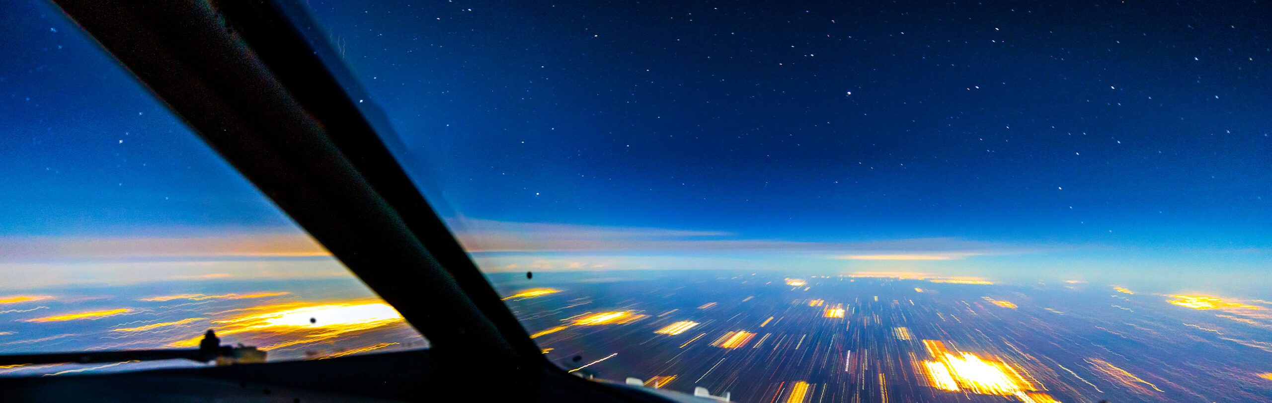 view out of the cockpit of a plane as it travels through a night sky, abstract lines and blocks of bright yellow and orange light pass under and appear out into the horizon giving the impression of fast forward motion