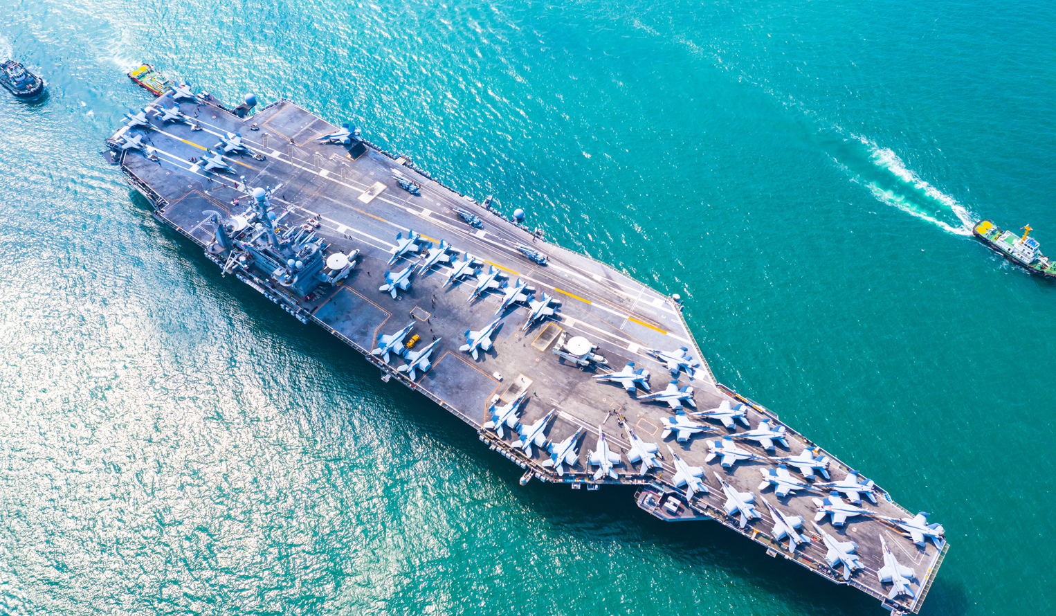 A US Navy carrier with planes on deck traveling as part of a fleet